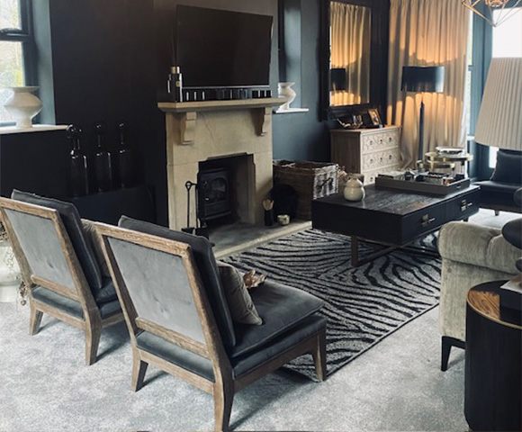 A stylish living room scene featuring a decorative table with white hydrangea blooms in a black vase, black candles, and a textured black frame, complemented by soft pillows on a dark sofa.